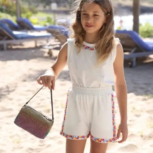 Girl wearing white summer top and shorts with rainbow gem trim, holding a glittery purse – outfit available at Togs, GCC kidswear reseller +Post Title + Separator + Category + Separator + Site Title